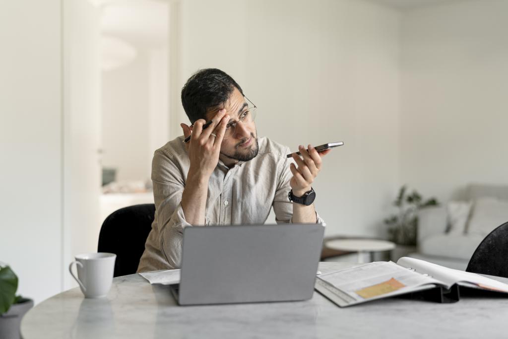 Man framför en dator och med telefon i handen